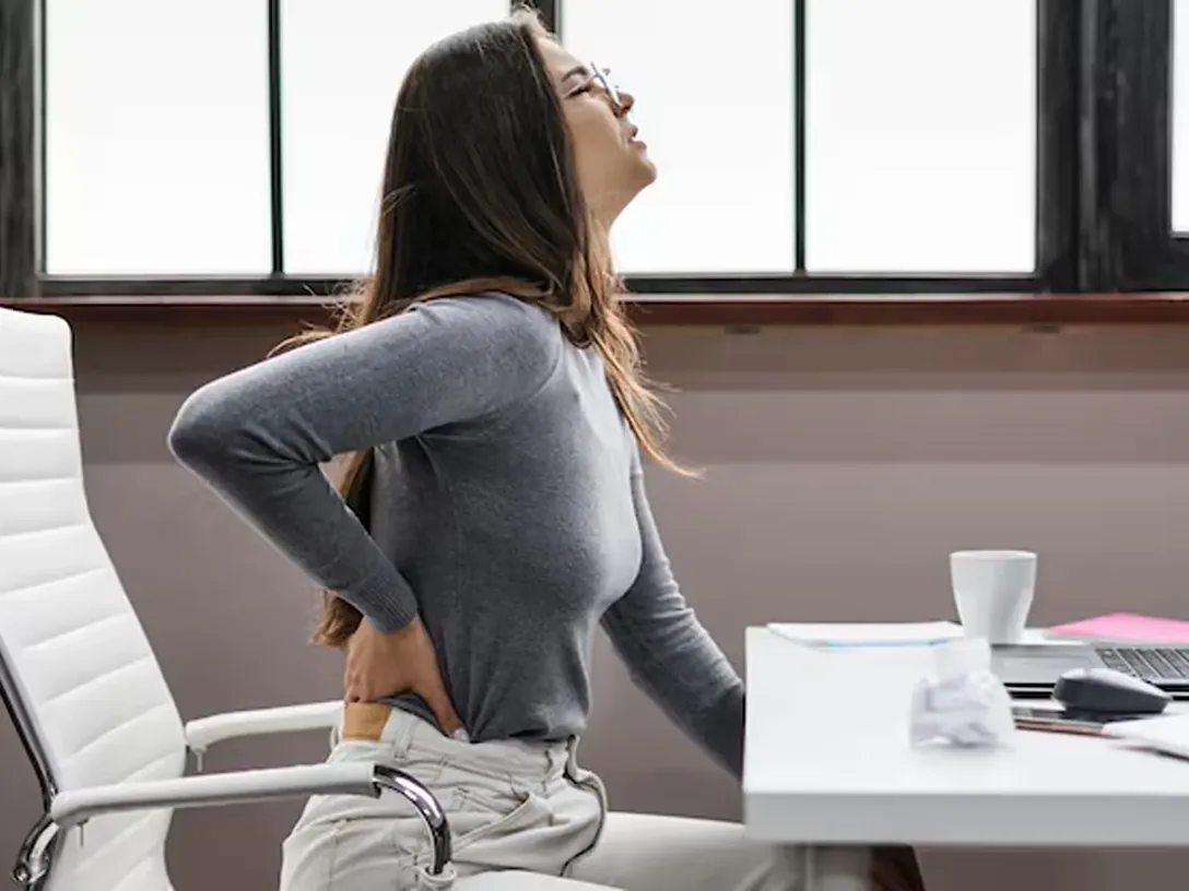 Woman at a desk holding her lower back