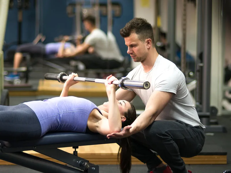 Trainer spotting a woman on a bench press