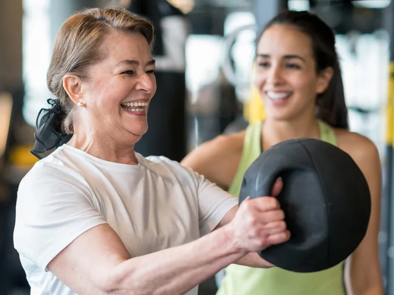 Woman lifting a medicine ball with a trainer in a gym