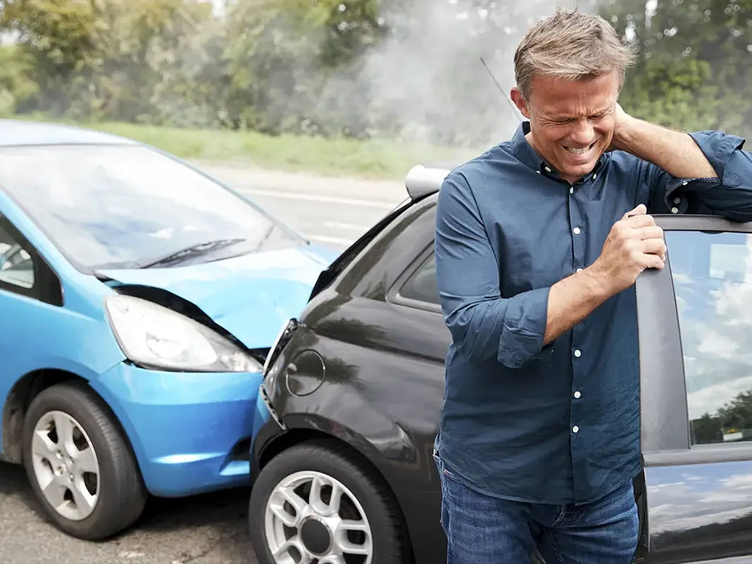 Man holding his neck beside two damaged cars