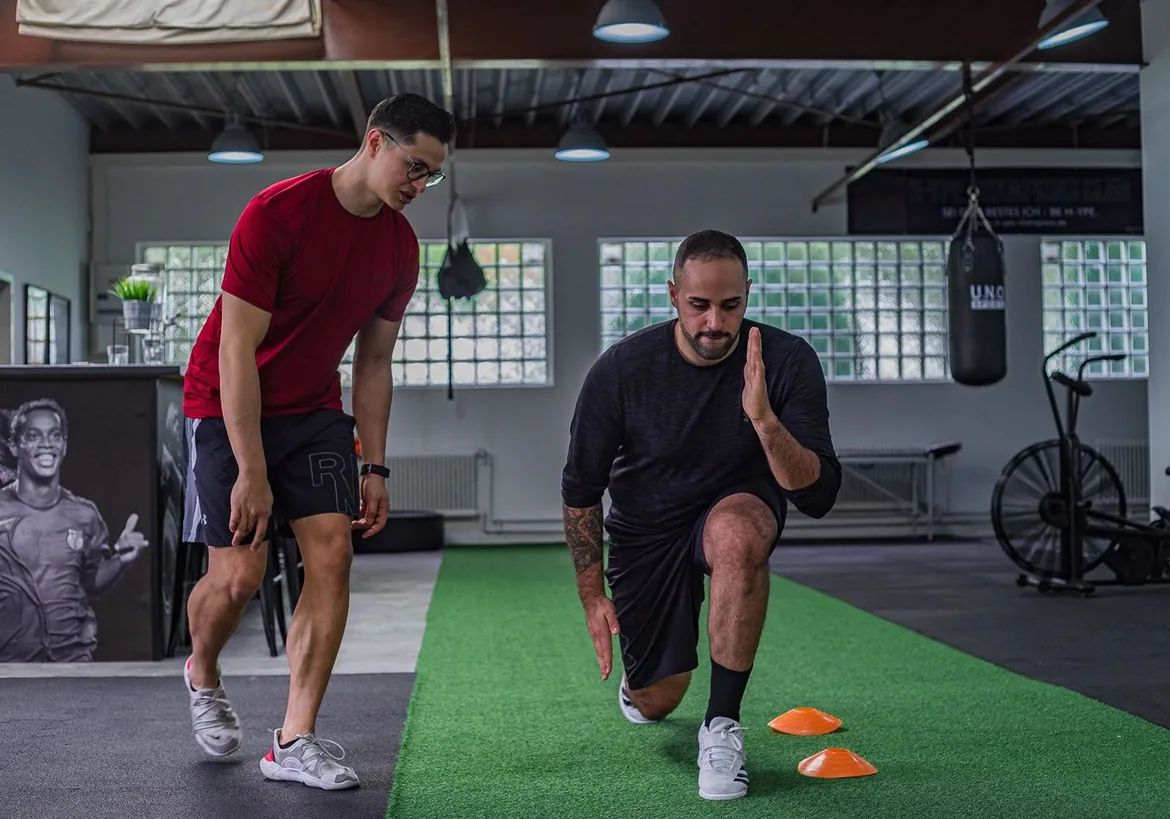 Trainer coaching a man through a lunge in a gym