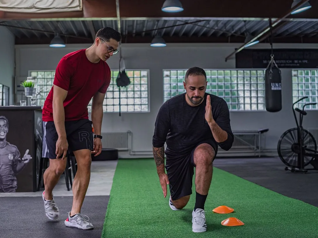 Trainer coaching a man through a lunge in a gym