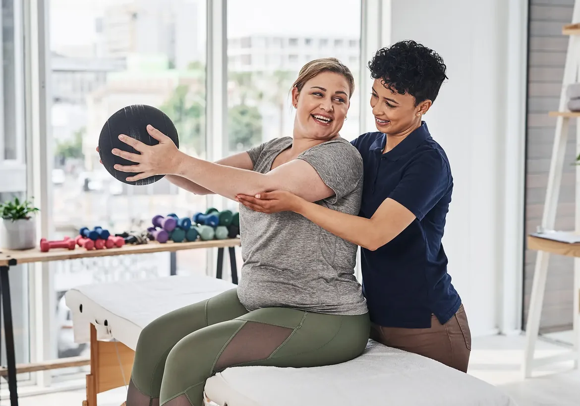 Clinician helping a woman lift a weighted ball