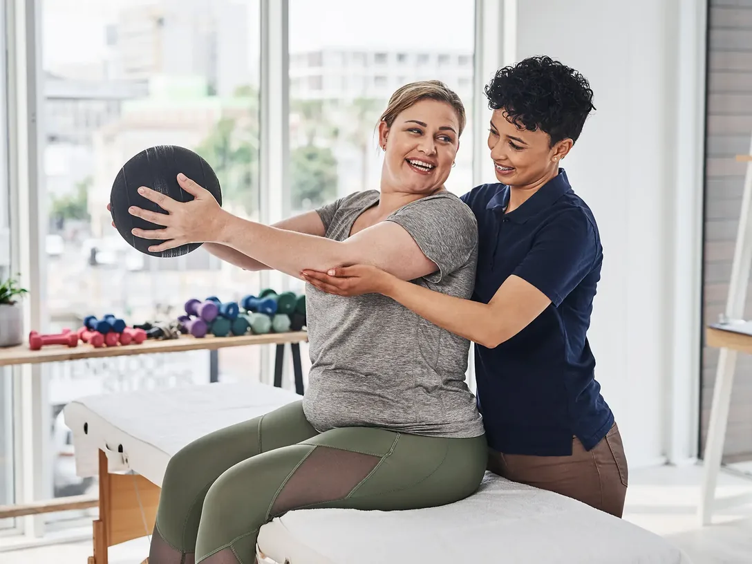 Clinician helping a woman lift a weighted ball