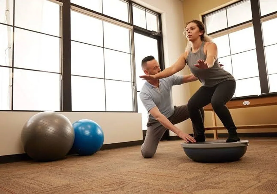 Clinician guiding a woman through a balance exercise on a half ball