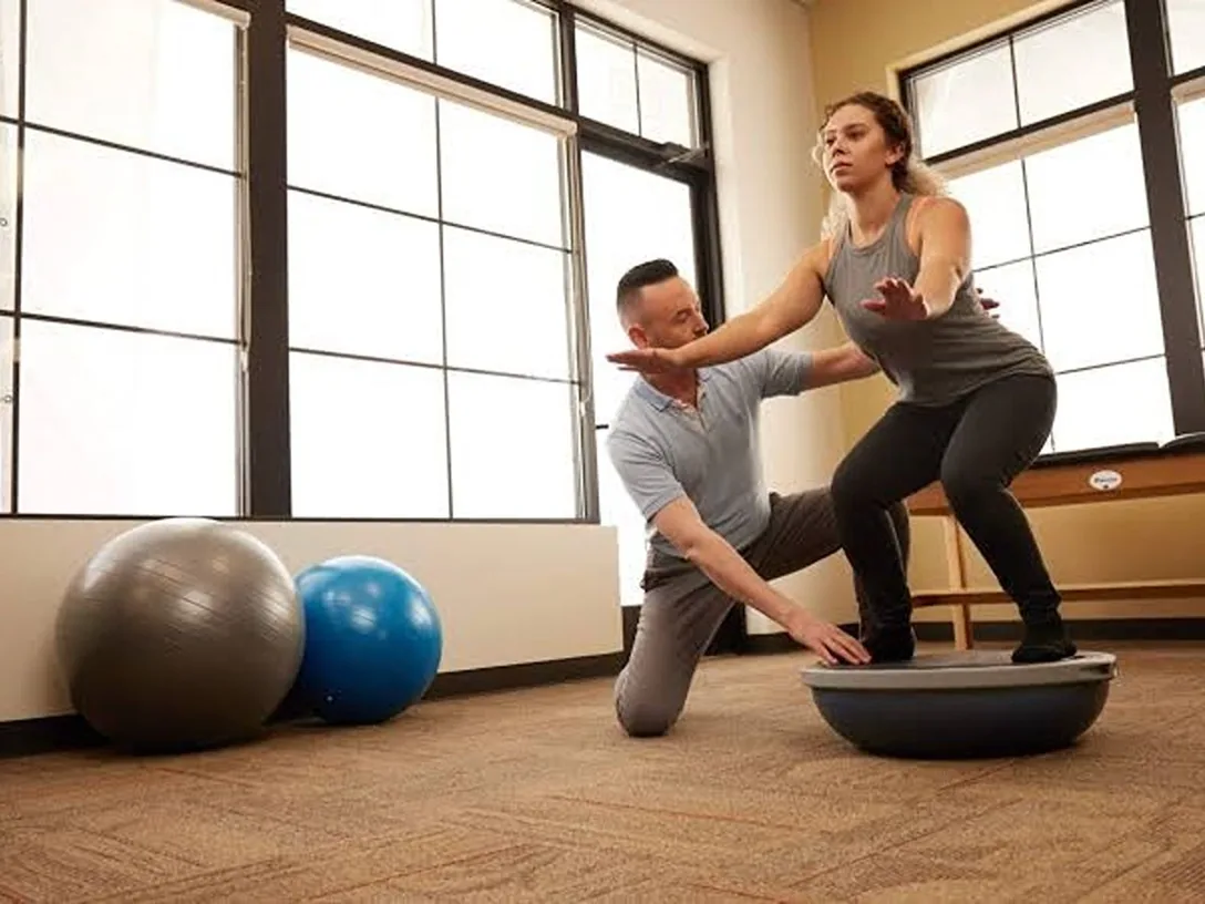 Clinician guiding a woman through a balance exercise on a half ball