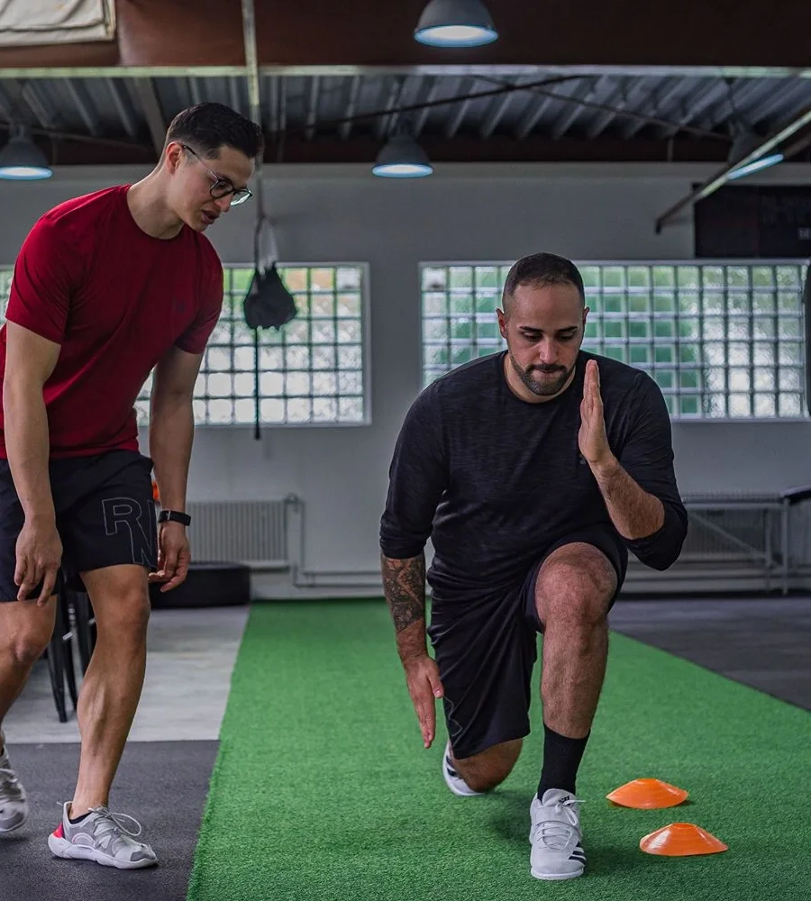 Trainer coaching a man through a lunge in a gym
