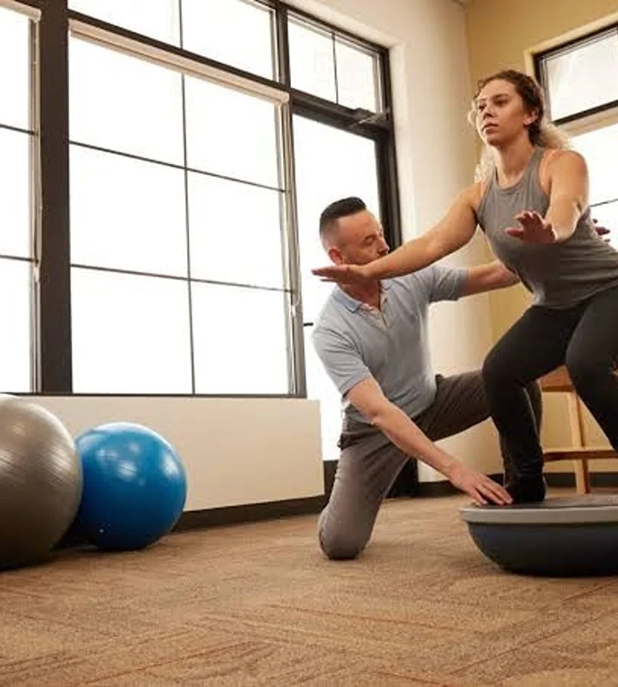 Clinician guiding a woman through a balance exercise on a half ball